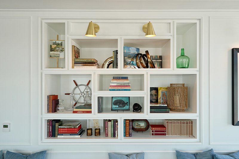 white built-in bookcase with books, ship wheel decor and sea glass vase